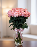 Bouquet of pink roses in a clear vase with a pink ribbon on a blurred background