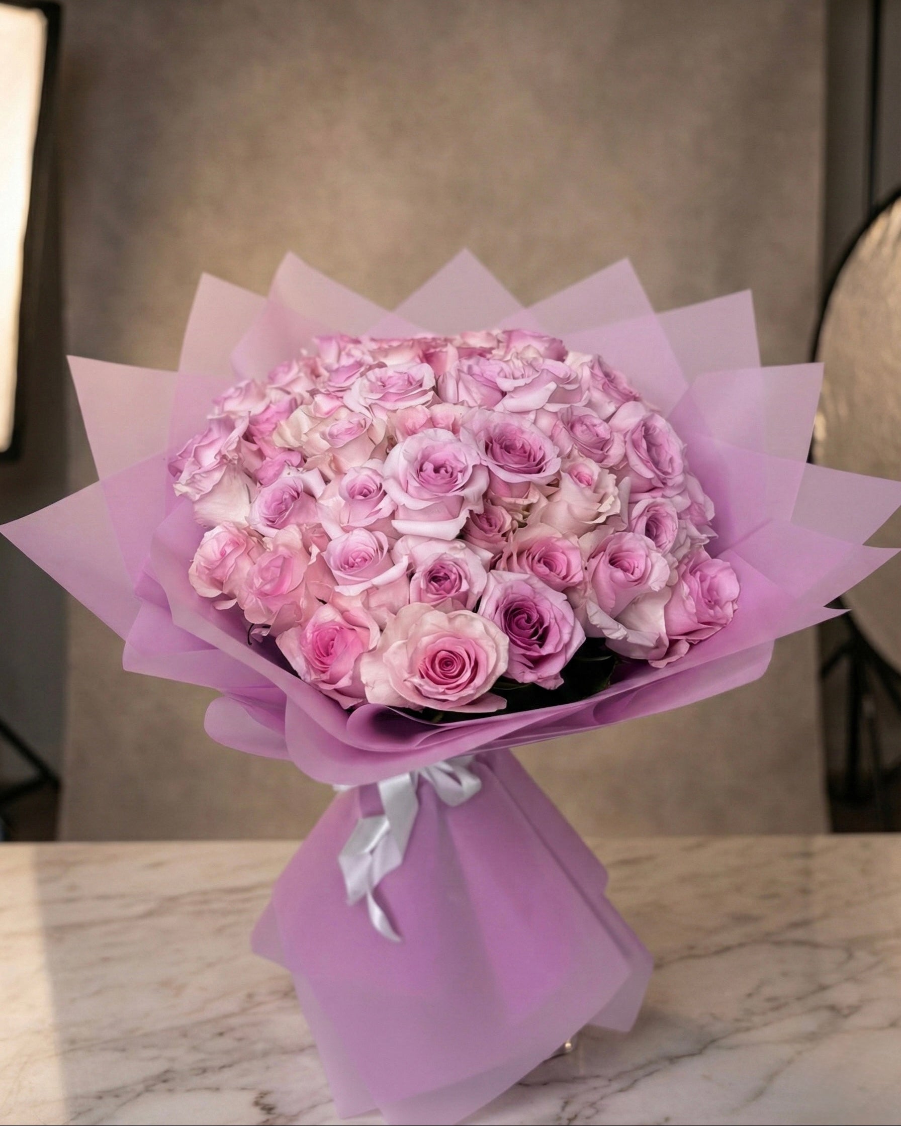 Bouquet of pink and white flowers wrapped in purple paper on a marble surface.