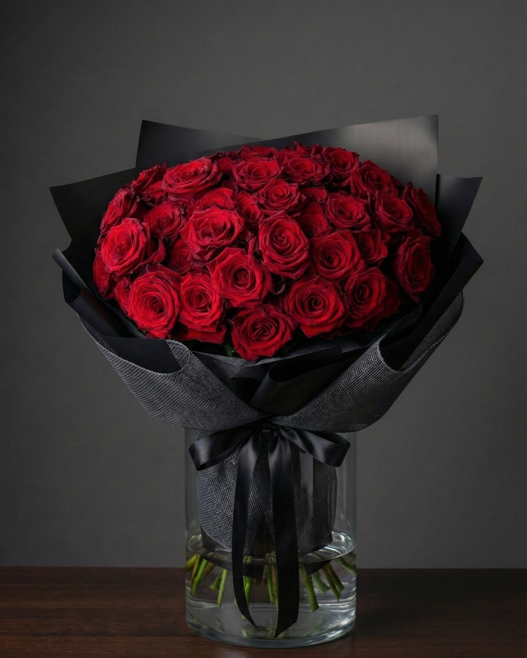 Bouquet of red roses wrapped in black paper with a clear vase on a dark background
